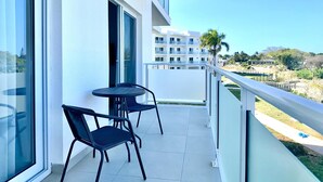Ein Balkon mit zwei Stühlen und einem Tisch, mit Blick auf ein Wohngebiet mit weißen Gebäuden und einer Palme.