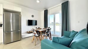 A modern kitchen with a built-in refrigerator, a dining area with a table and chairs, and a teal sofa.