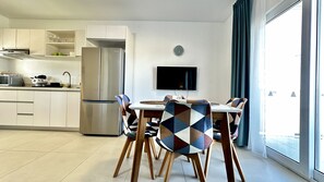 A modern kitchen with a built-in refrigerator, a dining table with patterned chairs, and a wall-mounted TV.