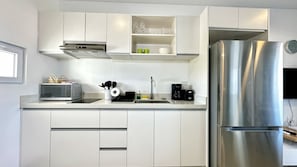 A modern kitchen with white cabinetry, a stainless steel refrigerator, a microwave, a toaster, and a coffee maker.