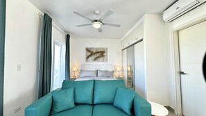 A hotel room with a bed, a ceiling fan, a wall-mounted artwork, and a window with curtains.