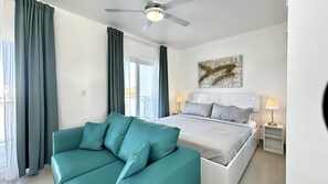 Ein modernes Schlafzimmer mit einem Bett, einer Couch, einem Deckenventilator und einem Fenster mit Vorhängen.