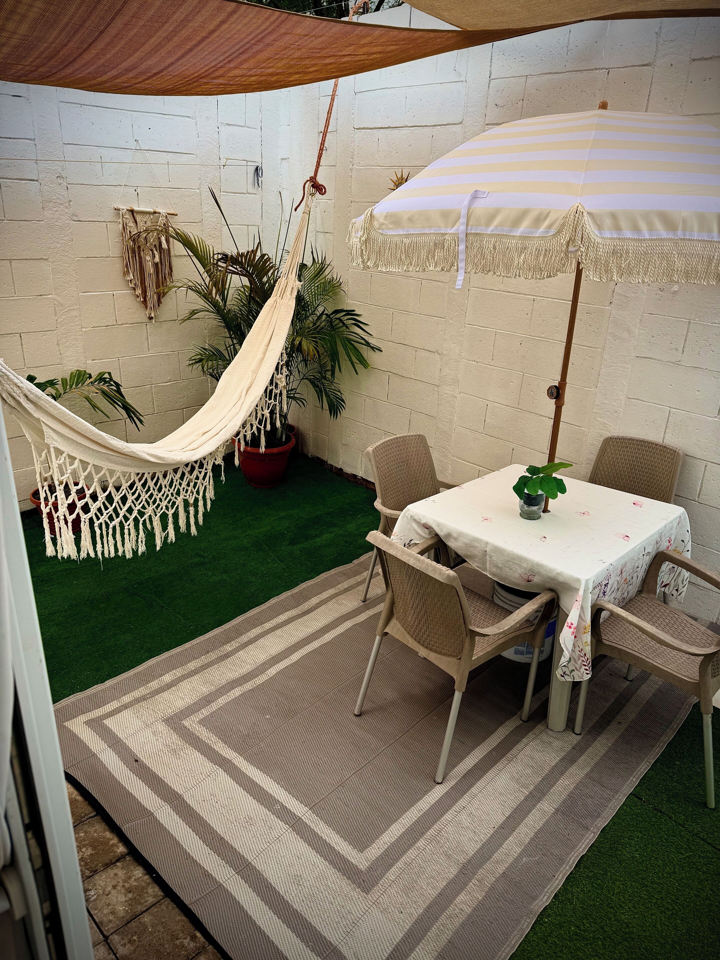 Un patio con una mesa, sillas, una hamaca y una planta en maceta.