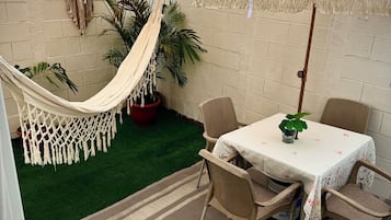 Un patio con una mesa, sillas, una hamaca y una planta en maceta.
