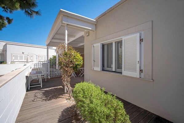 A covered outdoor area with a wooden deck, a small tree, and a white fence.