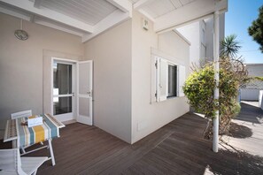 A covered patio area with a table and chairs, a small plant, and a door leading to a room. - WePuglia - Residence Cala Paura – Apt. Delfini (Polignano a Mare)