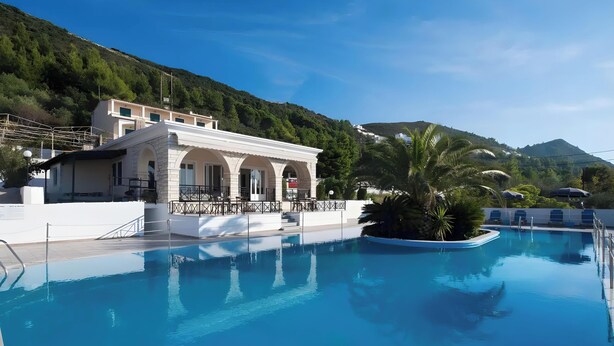 A swimming pool with a building adjacent to it, surrounded by greenery and hills.