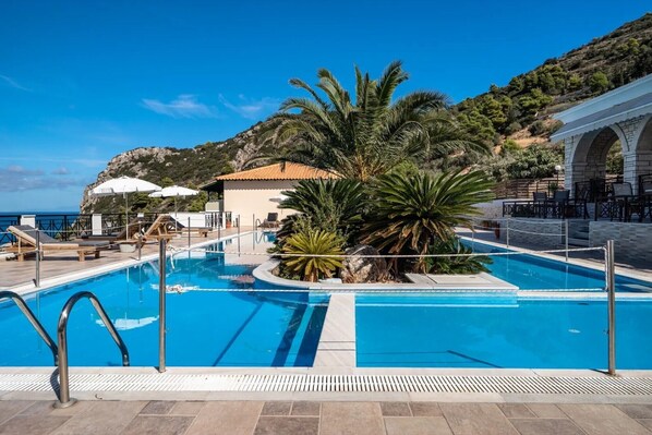 Zona de piscina con sillas de descanso, una palmera y un edificio con techo de tejas.