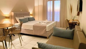 A hotel room with a bed, a dining table, chairs, a sofa, a TV, and a window with curtains.