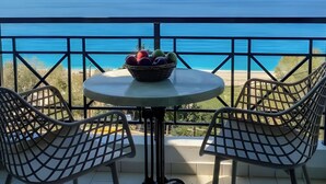 A balcony with a table and chairs, a basket of fruit, and a view of the sea.