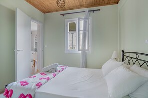 A bedroom with a bed, a window, a door, and a wooden ceiling.