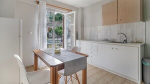 Een compacte keuken met een eethoek, witte kastjes en uitzicht door een open deur.