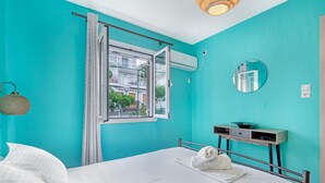Een kamer met een bed, een raam met gordijnen, een nachtkastje met spiegel en een airconditioning.