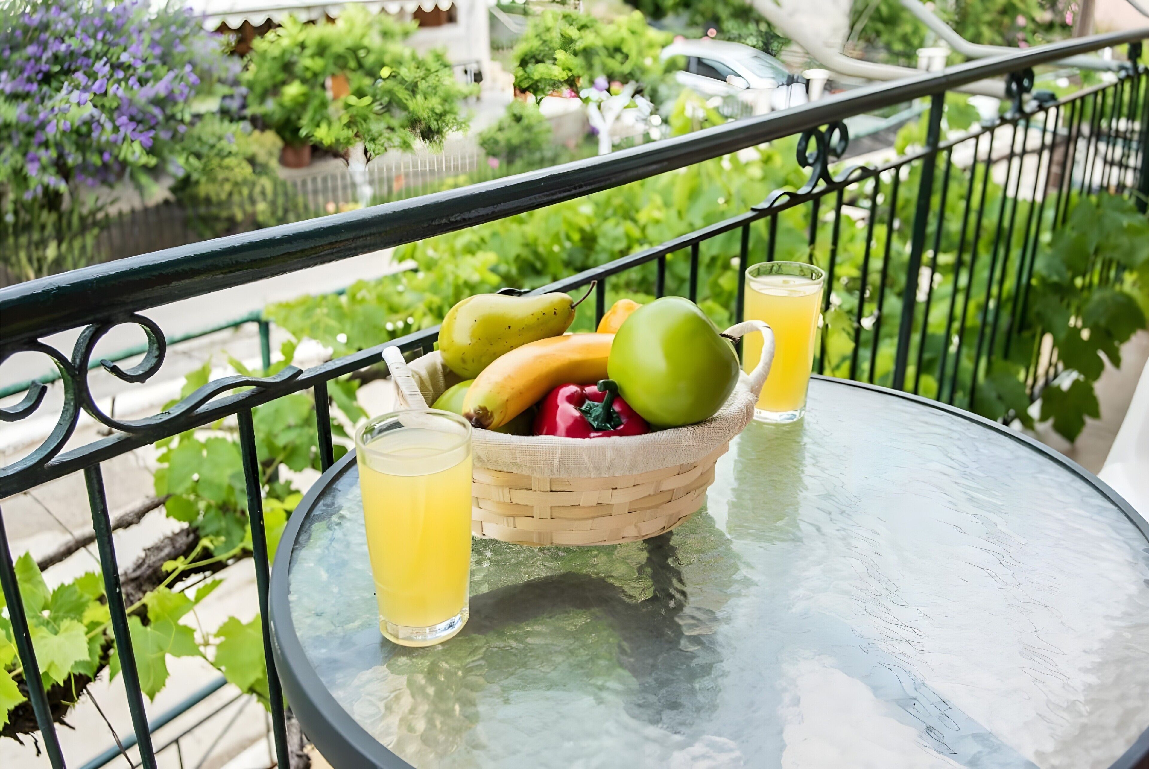 A glass table with a wicker basket containing fruits and a glass of juice.