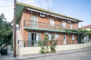 Een gebouw met twee verdiepingen, een balkon, airconditioningsapparaten en een groene metalen reling.