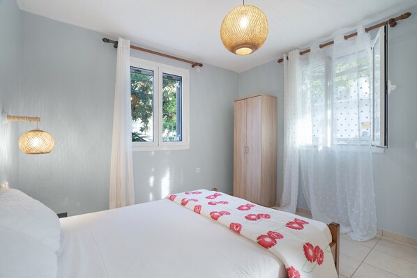 Een slaapkamer met een bed, een kledingkast, een raam met gordijnen en een hanglamp.