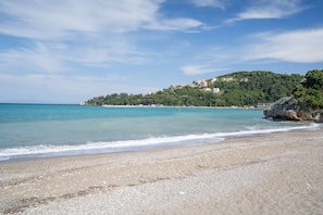 A beach with clear water, a sandy shore, and buildings on a hillside in the background. - Apartment 'Two-Bedroom' with Shared Garden, Wi-Fi and Air Conditioning (Póros Kefalonias)