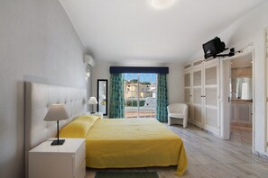 Een hotelkamer met een bed, nachtkastjes, een stoel, een kledingkast en een balkon met gordijnen.
