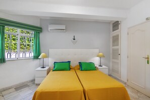 A double bed with yellow bedding, two bedside tables with lamps, a white headboard, a window with green curtains, and a white door with a lock. - Villa 'Rebelo' with Private Pool, Private Garden and Wi-Fi (Albufeira)