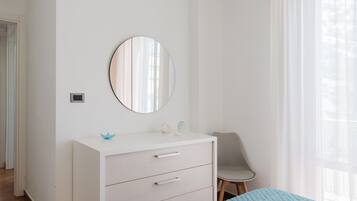 A bedroom with a white dresser, a round mirror, a chair, and a bed with a blue bedspread.