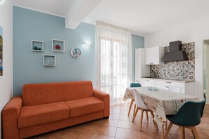 A living room with a sofa, dining table, chairs, and a kitchen area with cabinets and a tiled backsplash. - Apartment 'Kairos' with Shared Pool, Wi-Fi and Air Conditioning (San Vito Lo Capo)