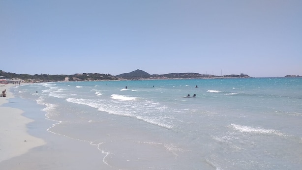 Ein Strand mit klarem Wasser, darin schwimmende Menschen und ein Berg in der Ferne.