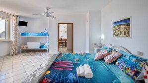 A bedroom with a bunk bed, a bed with a colorful ocean-themed bedspread, a ceiling fan, a TV mounted on the wall, and a window with curtains. - Holiday Home 'Solea Panoramic Sea View' with Sea View, Wi-Fi and Air Conditioning (porto cesareo)
