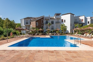 Une piscine entourée de bâtiments à plusieurs étages dotés de balcons, avec des chaises longues et des parasols à proximité.