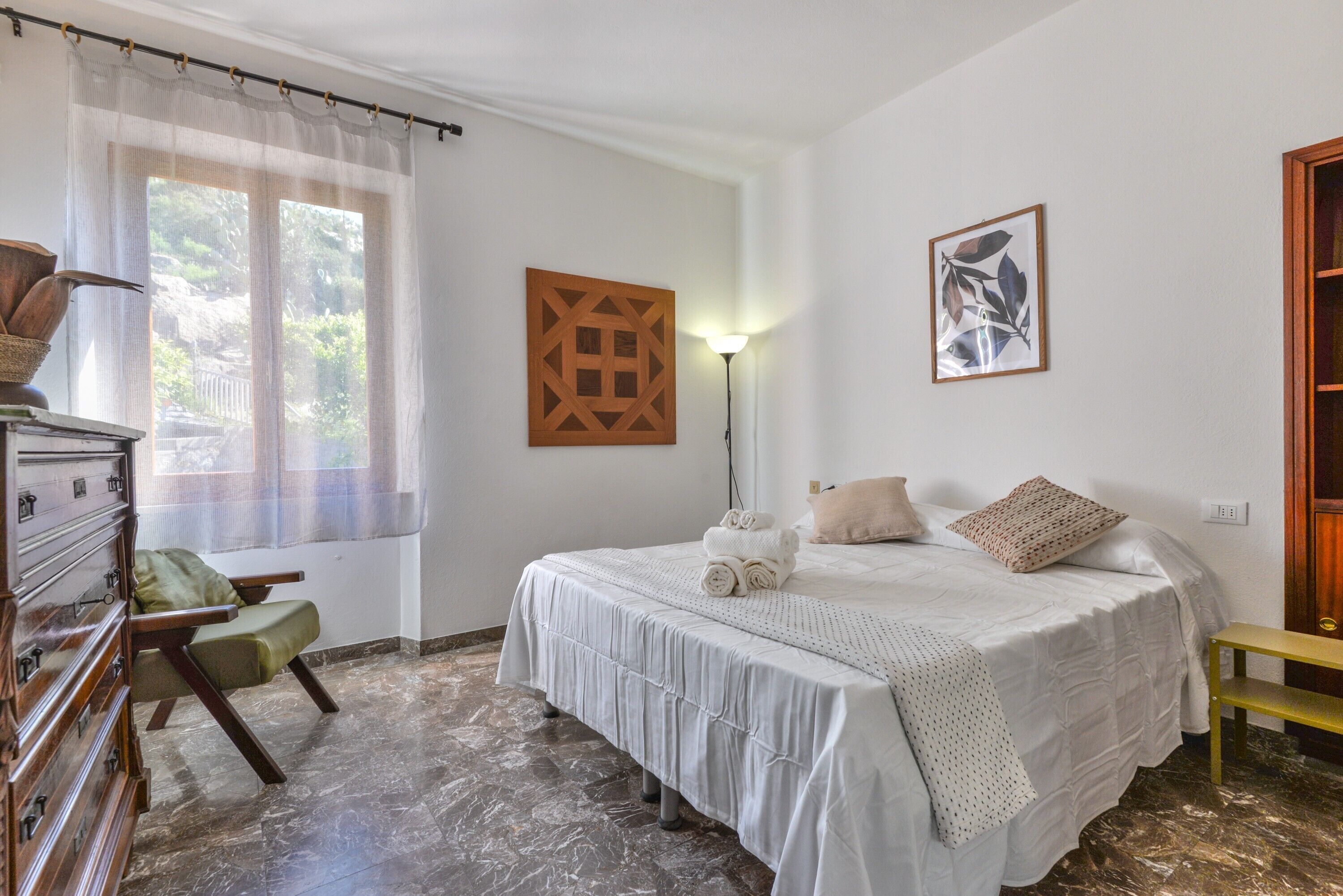 Ein Schlafzimmer mit einem Bett, einem Sessel, einem Schminktisch, einer Lampe und Bildern an den Wänden.