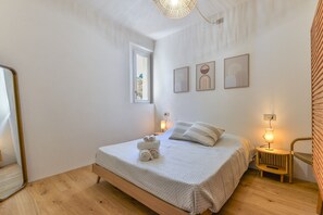 A bedroom with a bed, bedside lamps, a mirror, and a window.