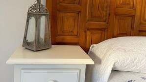 Un lit recouvert d’une couvre-lit à motifs floraux, une table de chevet avec un tiroir et une lanterne décorative.