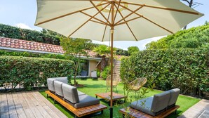 Une terrasse extérieure avec des meubles en bois, un grand parasol et une pelouse bien entretenue.