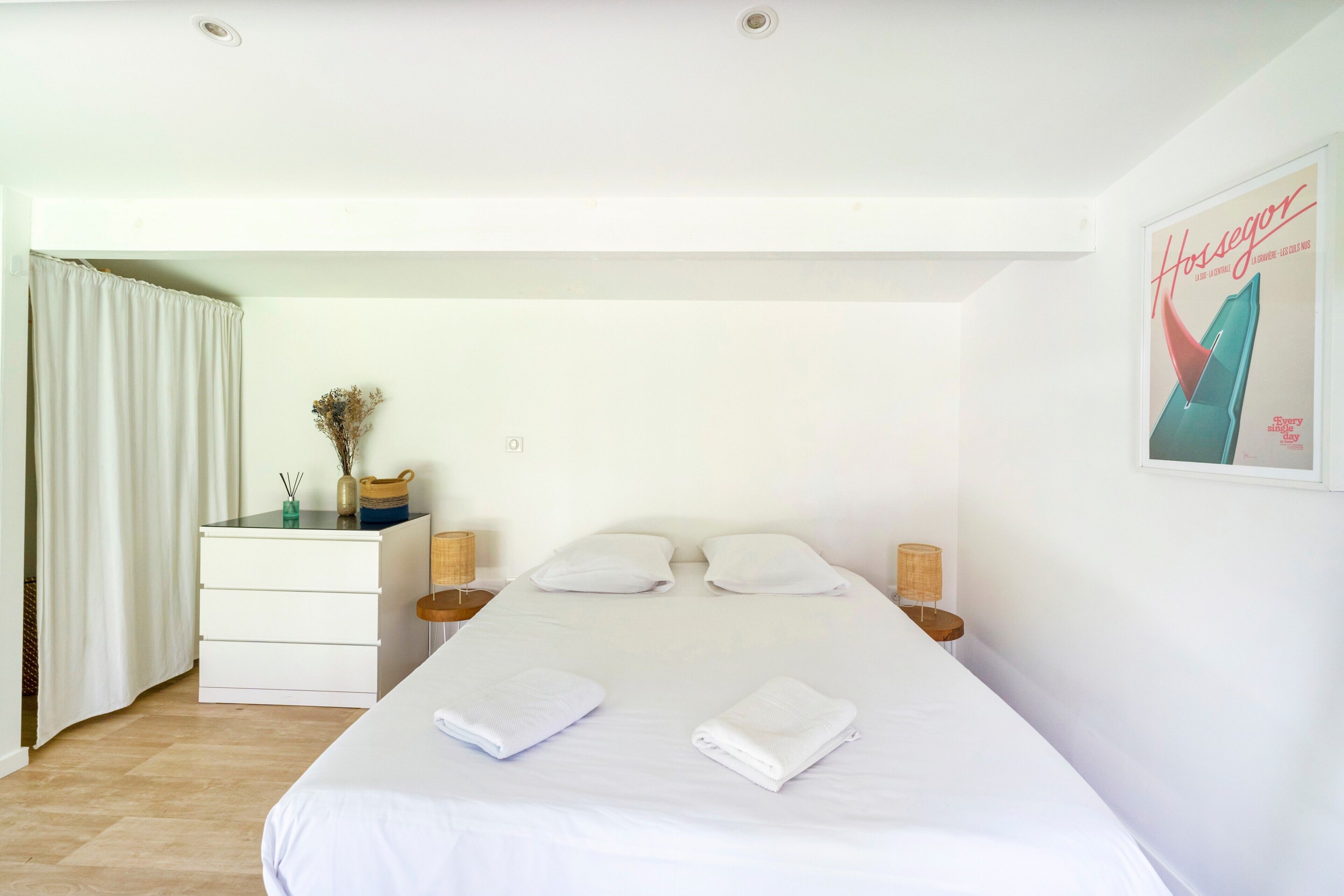 A bedroom with a bed, two bedside tables, a dresser, a window with curtains, and a poster on the wall.
