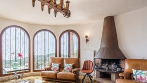 Una sala de estar con chimenea, sofás de cuero, una mesa con un florero y ventanas arqueadas amplias.