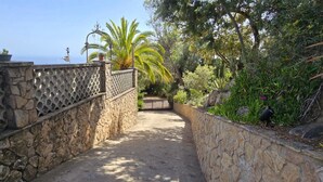 Un sendero de piedra que conduce a una puerta, rodeado de abundante vegetación y vista al mar.