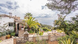 Un edificio blanco con techo de piedra, un patio con plantas y vista al mar.