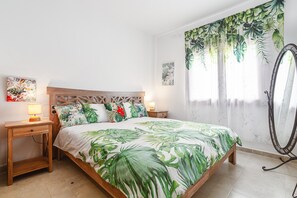 Ein Schlafzimmer mit Bett, Nachttischen, einem Spiegel und tropisch gestalteten Vorhängen.