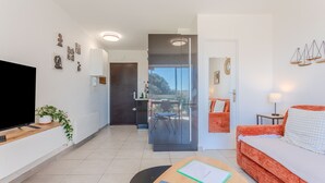 Ett modernt vardagsrum med en platt-TV, ett träbord med tidningar, en röd soffa och en glasdörr som leder ut till en balkong.