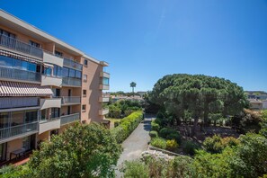 A multi-story residential building with balconies, a garden pathway, and a large tree.