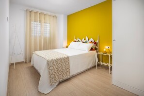 A bedroom with a bed, a bedside table with a lamp, a window with curtains, and a tripod stand.