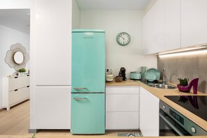 A modern kitchen with a teal refrigerator, white cabinetry, a stainless steel sink, and a clock on the wall.