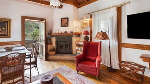 A cozy room with a fireplace, a red armchair, a dining table with chairs, and a television. - Vacation 'Main House' with Mountain View, Wi-Fi and Air Conditioning (Vega de San Mateo)