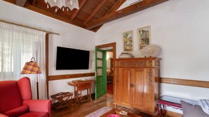 A living room with a red sofa, wooden cabinet, and a television mounted on the wall. - Vacation 'Main House' with Mountain View, Wi-Fi and Air Conditioning (Vega de San Mateo)