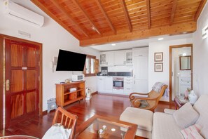 A living room with a sofa, wooden coffee table, TV, and a kitchen area with cabinets and a microwave.