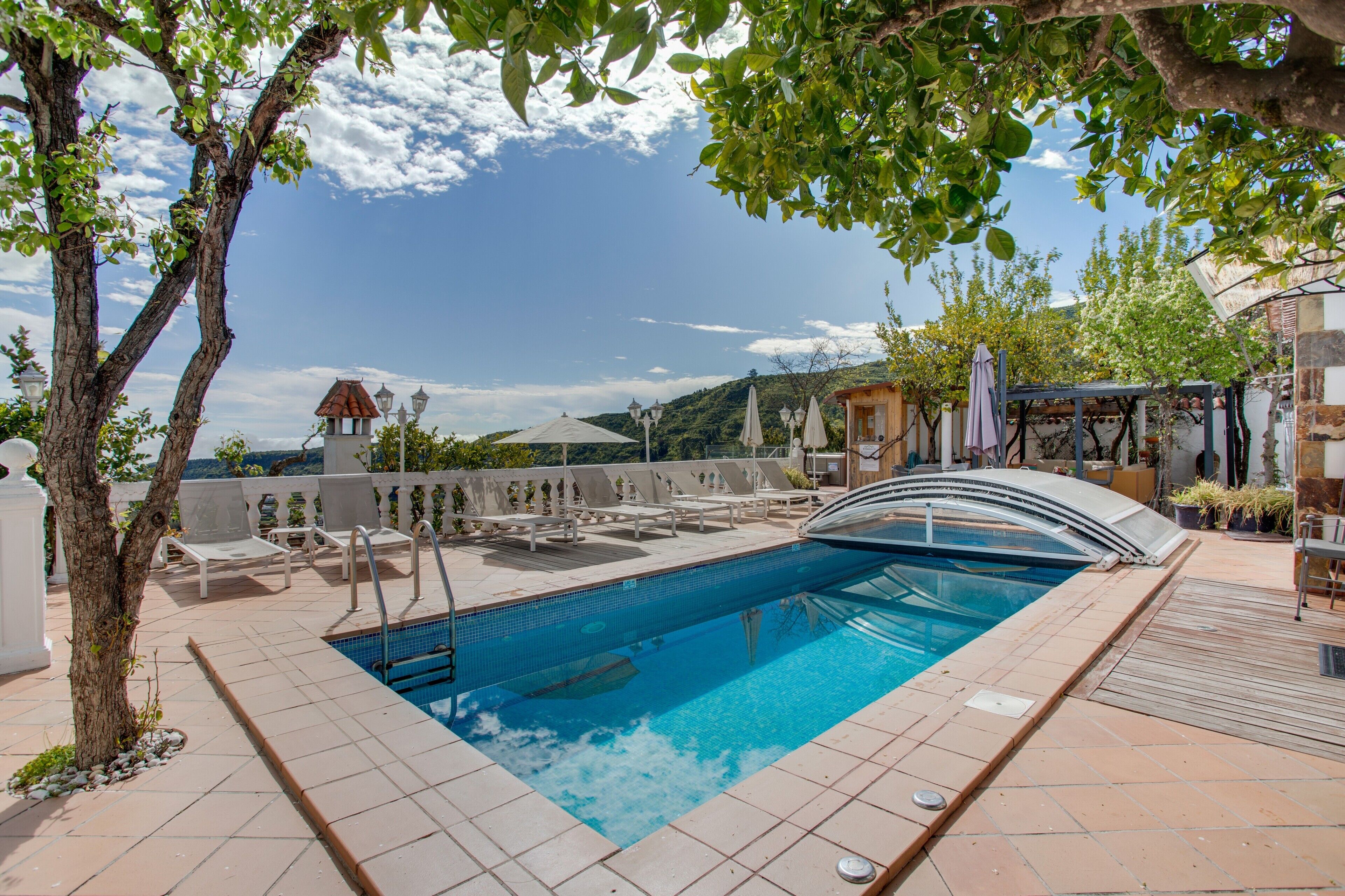 Una piscina de borde curvo, sillas de descanso y una pérgola con sombrillas.
