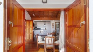 A wooden door leading to a dining area with a table and chairs, a kitchen in the background, and a ceiling with wooden beams. - Vacation 'Upper House' with Mountain View, Wi-Fi and Air Conditioning (Vega de San Mateo)
