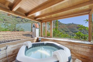 Un espace de détente en bois comprenant un bain à remous, de grandes fenêtres et une vue sur un paysage montagneux.