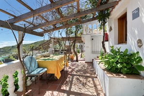 A covered outdoor seating area with a table and chairs, a pergola, and a view of the landscape.