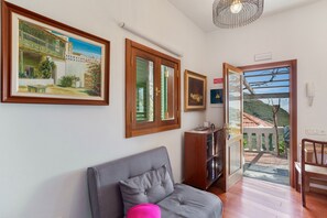 A room with a grey sofa, wooden floor, a door leading to a balcony, and framed artwork on the wall.