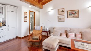 Una habitación con techo de madera, paredes blancas, un sofá, una silla, una mesa y cuadros enmarcados.